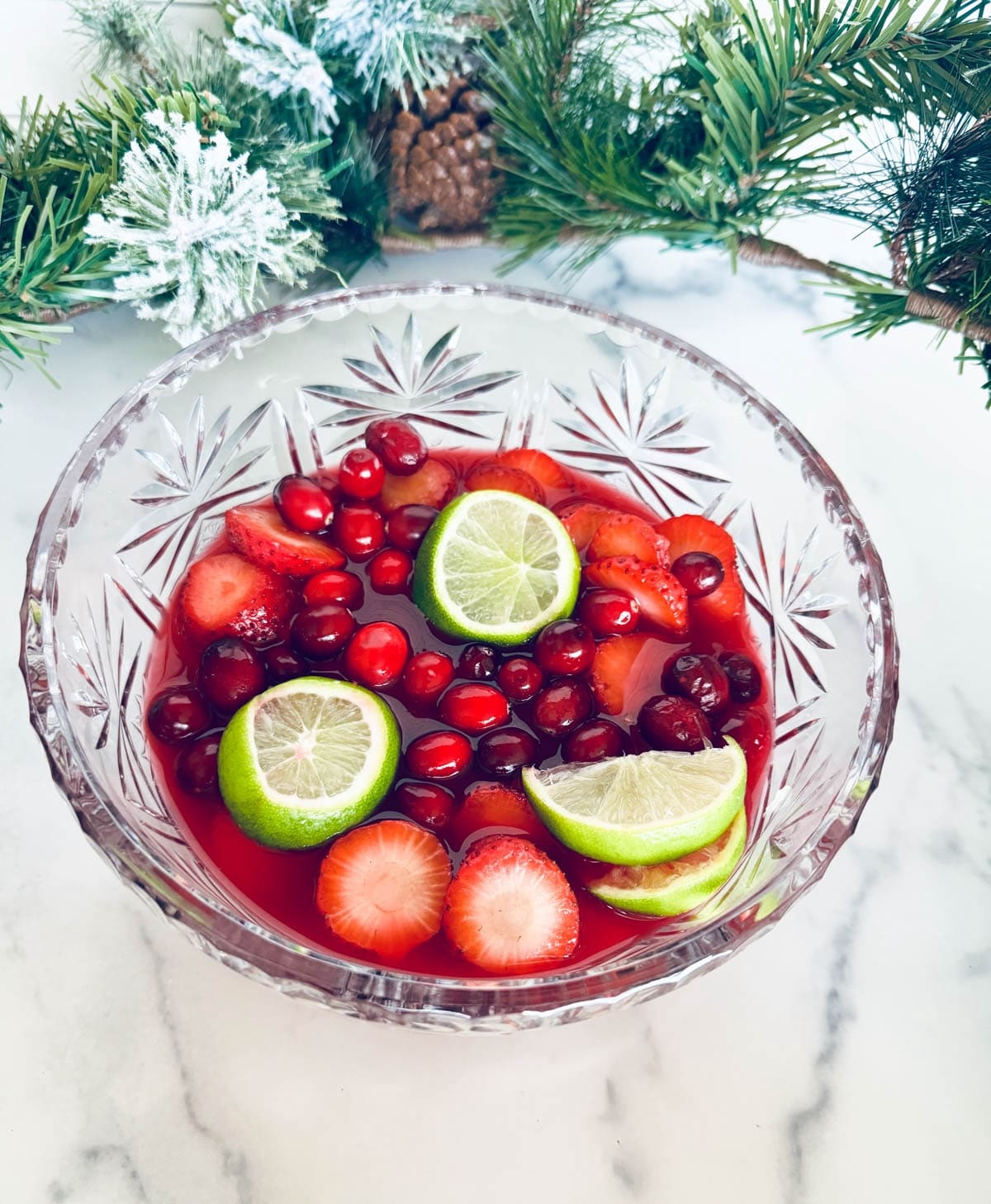 Juice and fruits in a glass punch bowl with Christmas greenery in background.