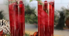 Tall glasses with cranberry juice and fresh cranberries and rosemary in a festive setting.