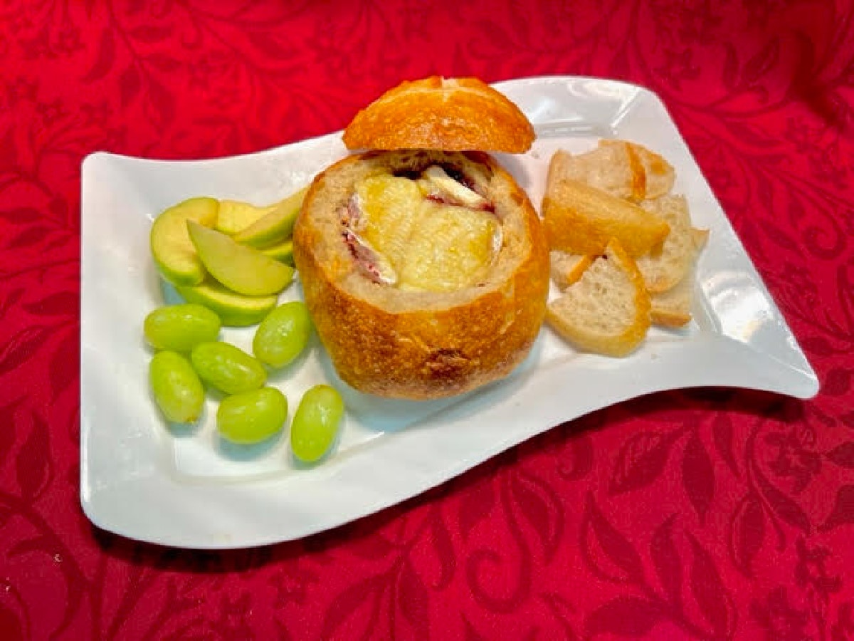 Brie cheese in bread bowl with fruit on side.