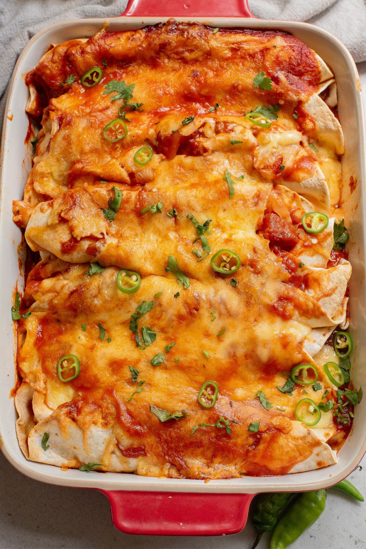 Chicken enchiladas in a casserole dish with diced jalapeno and green onion.