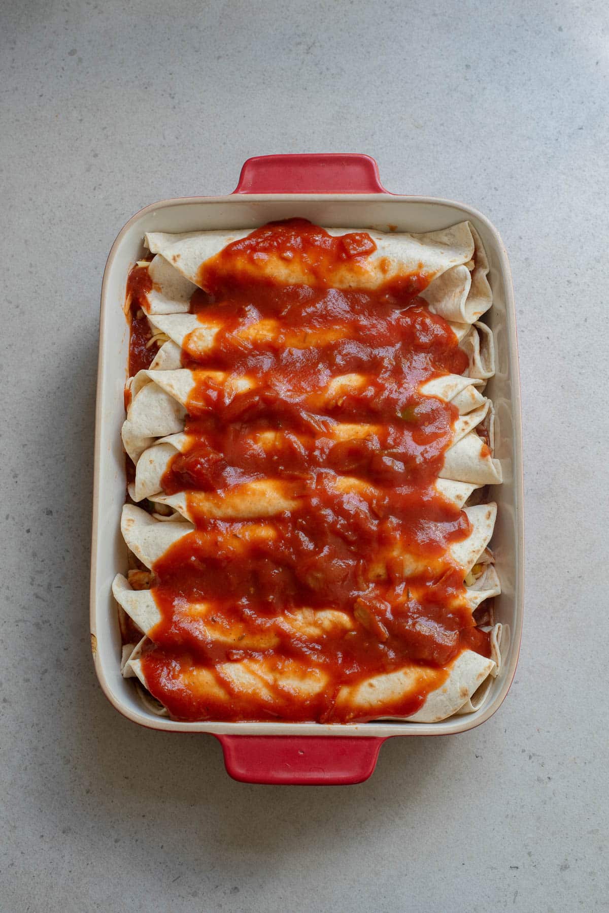 Enchiladas in a red baking dish covered with enchilada sauce before baking.