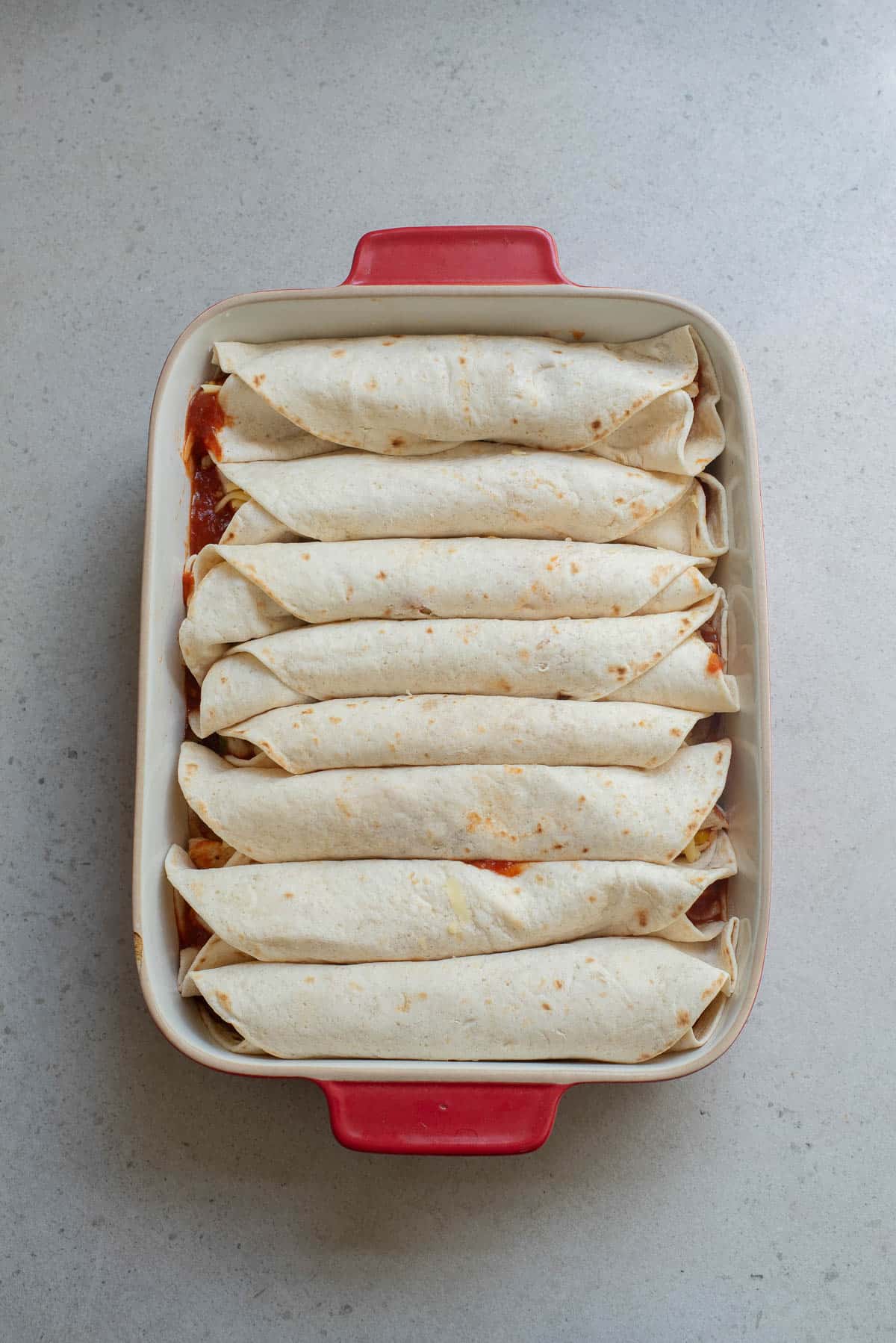 Tortillas filled with chicken and other filling rolled in a baking dish before baking.