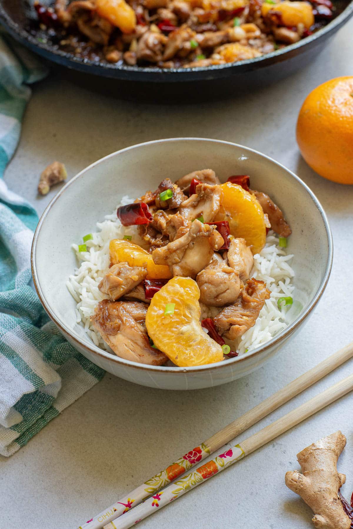 Mandarin orange chicken in a white bowl over rice and more in a cast iron pan above it.