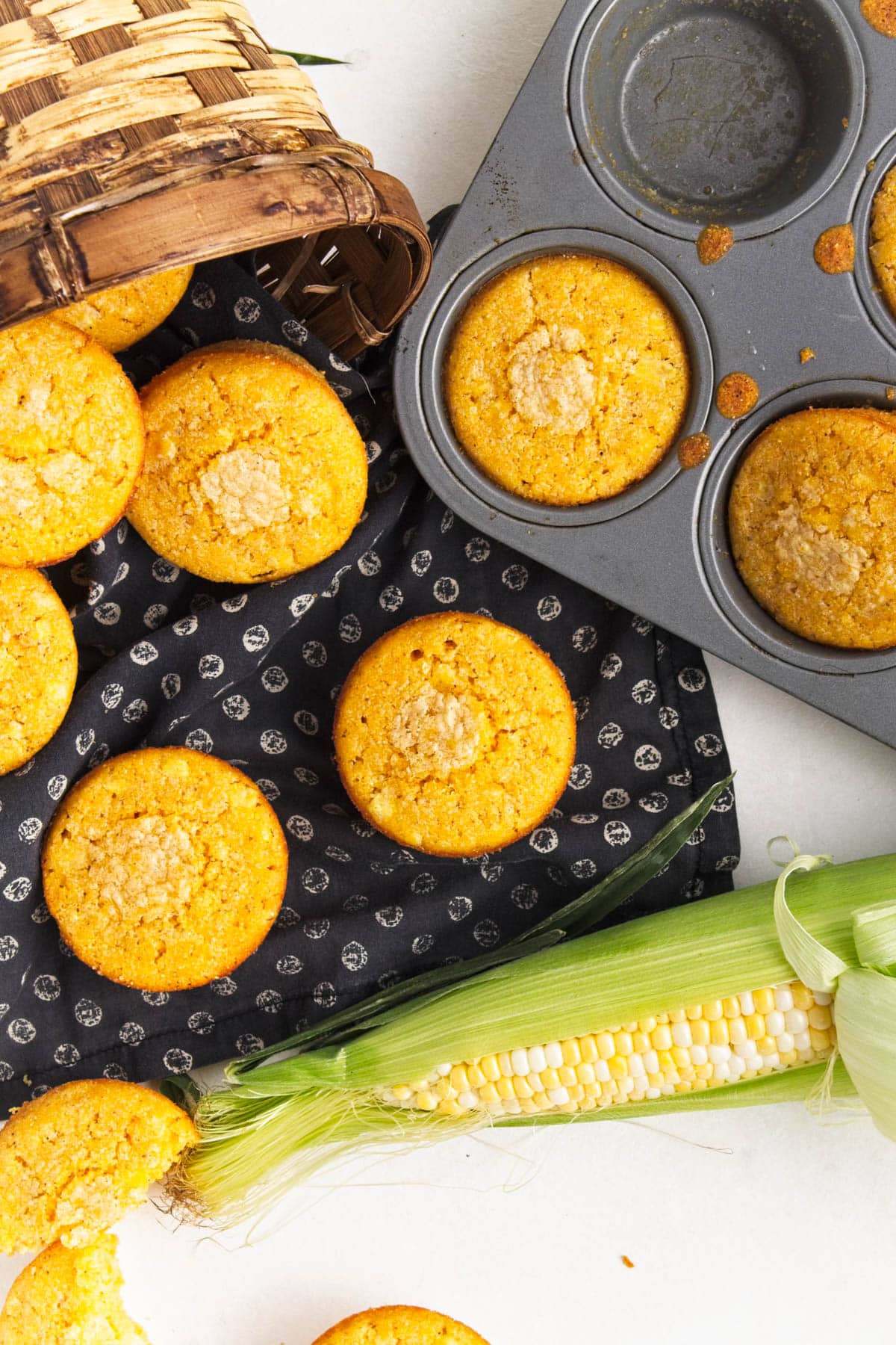 Cornbread muffins on black napkin and in muffin tin with corn on the cob.