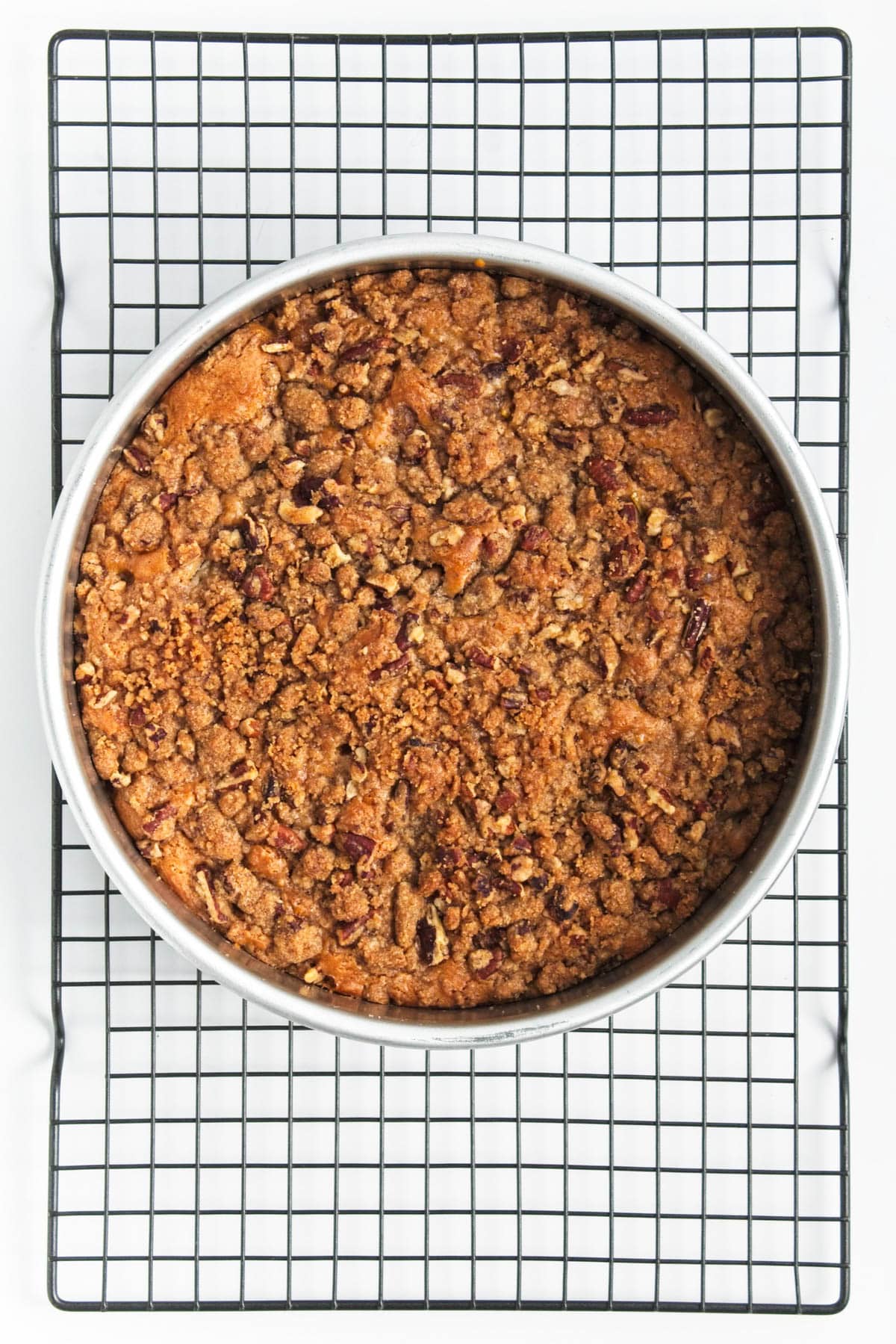 Coffee cake with cinnamon streusel in pan on wire rack.