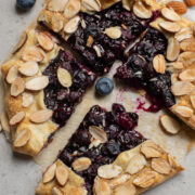 Blueberry galette dessert on a piece of parchment paper with one quarter sliced and pulled away.