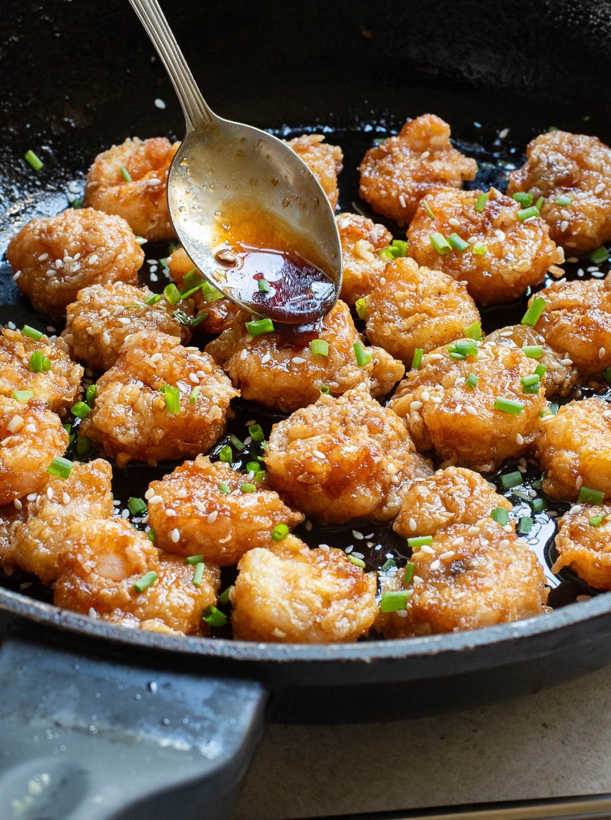 Fried shrimp with sauce and sesame seeds and chives in cast iron pan.
