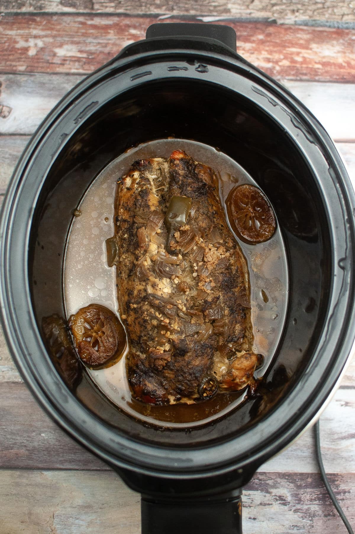 Cooked pork tenderloin with spices and limes in juices in slow cooker.