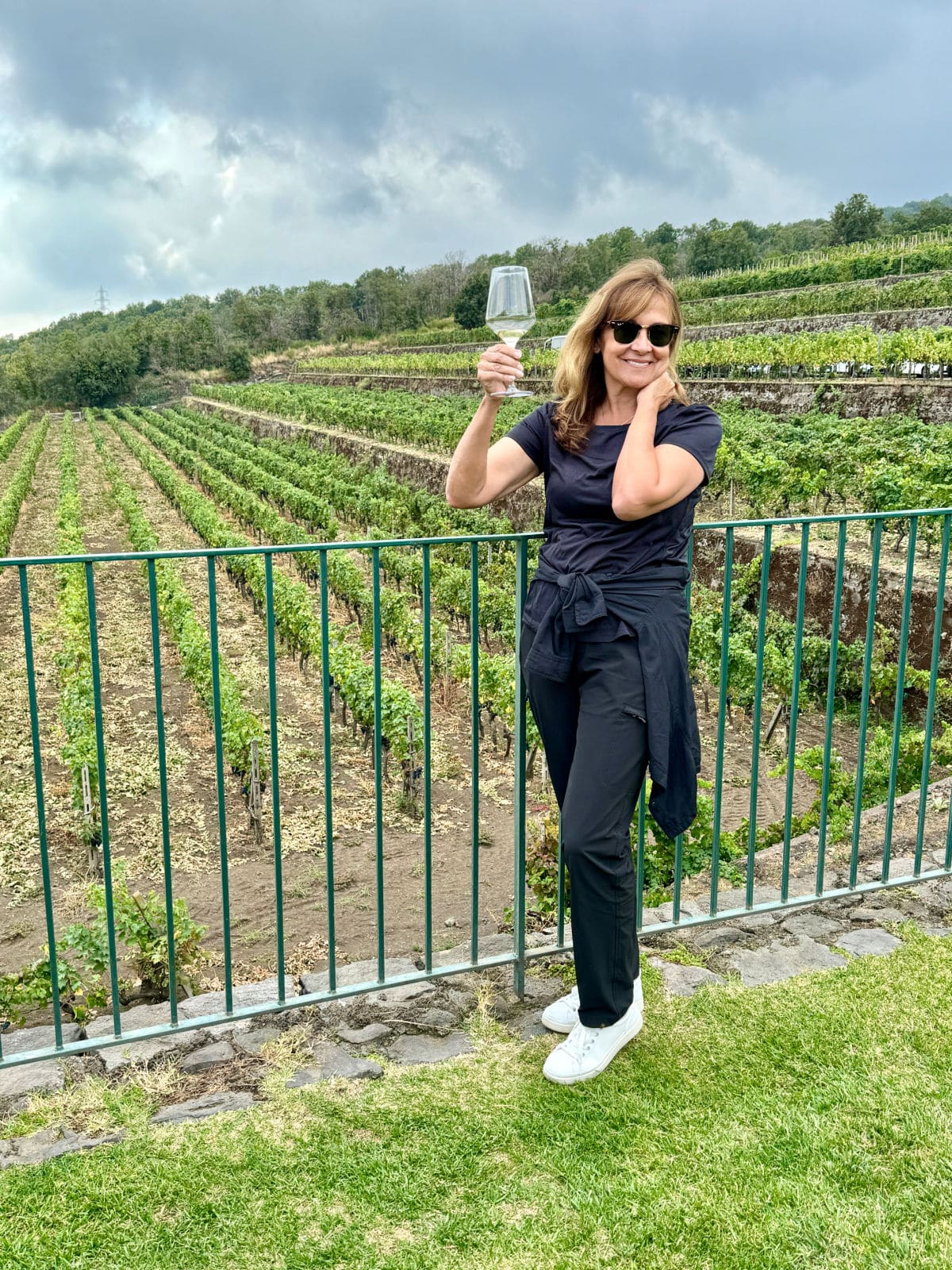 Woman holding wine glass up at vineyard.