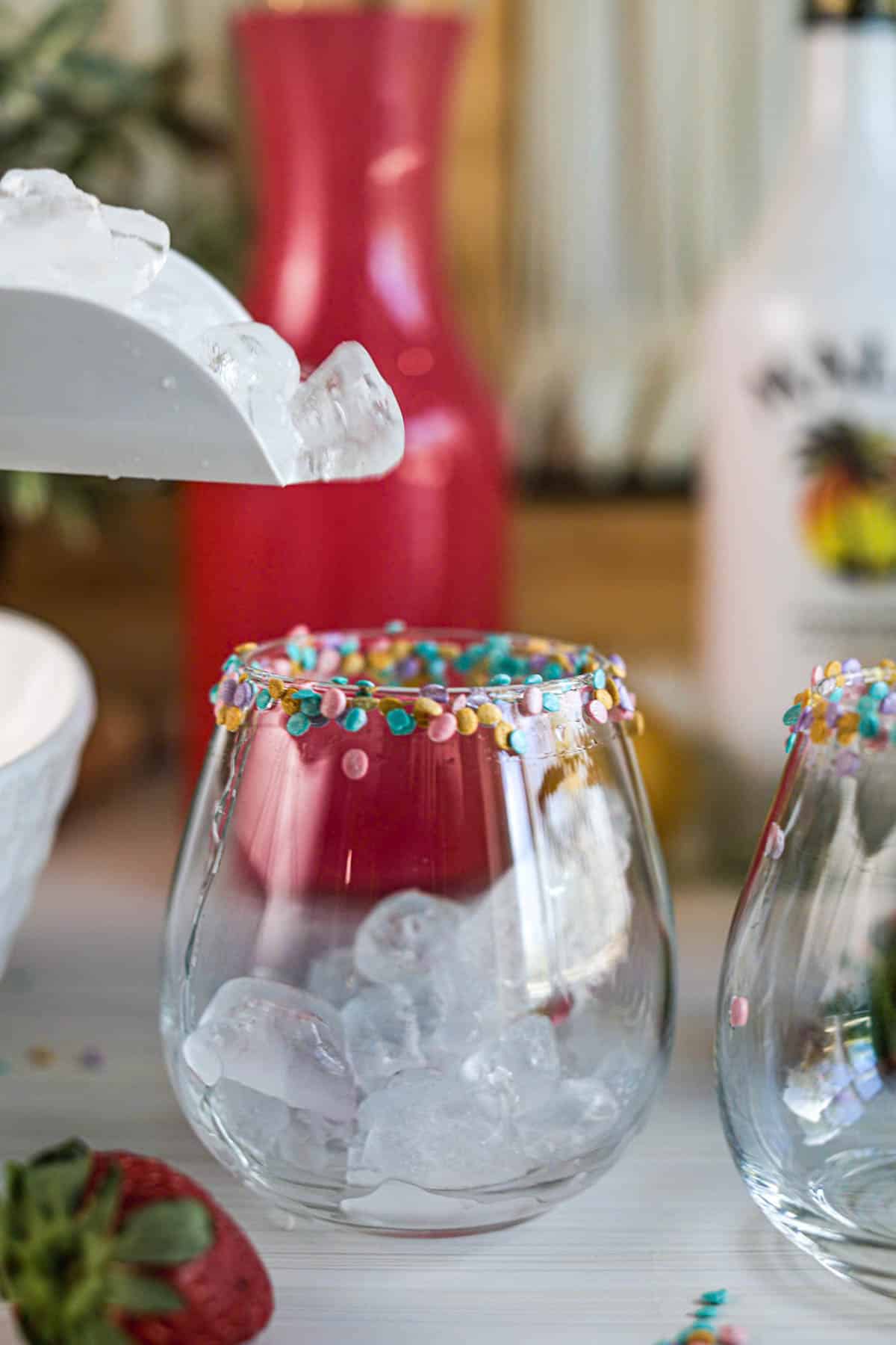 Pouring ice into glasses with sprinkles on rim.