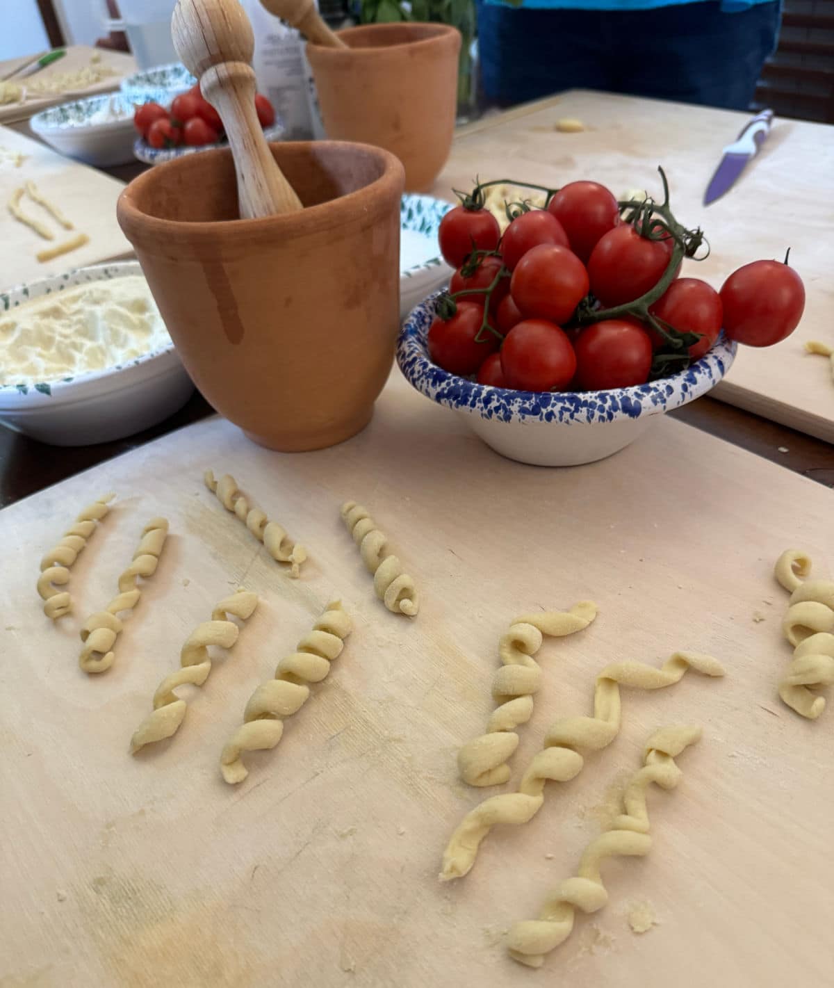 Mortar and pestle on a table with tomatoes and pasta.