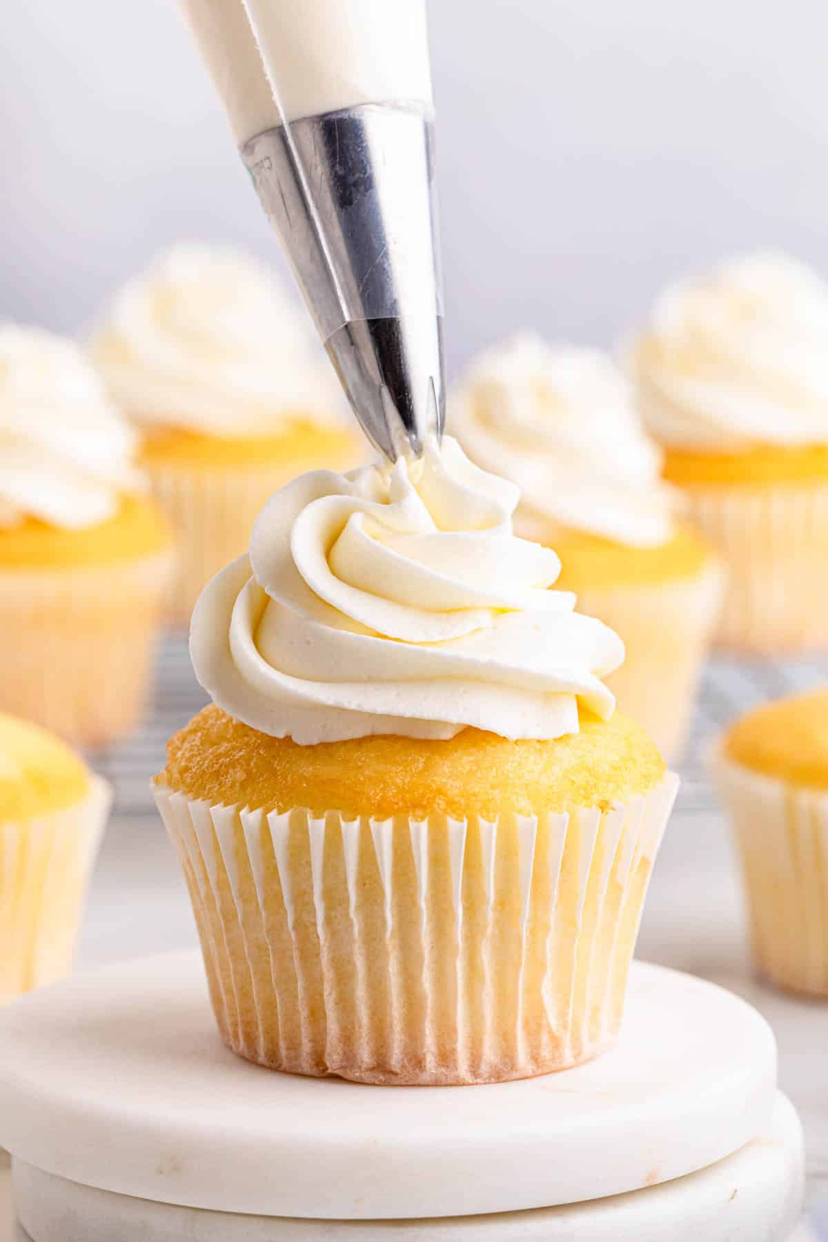 Whipped cream being piped onto a cupcake.