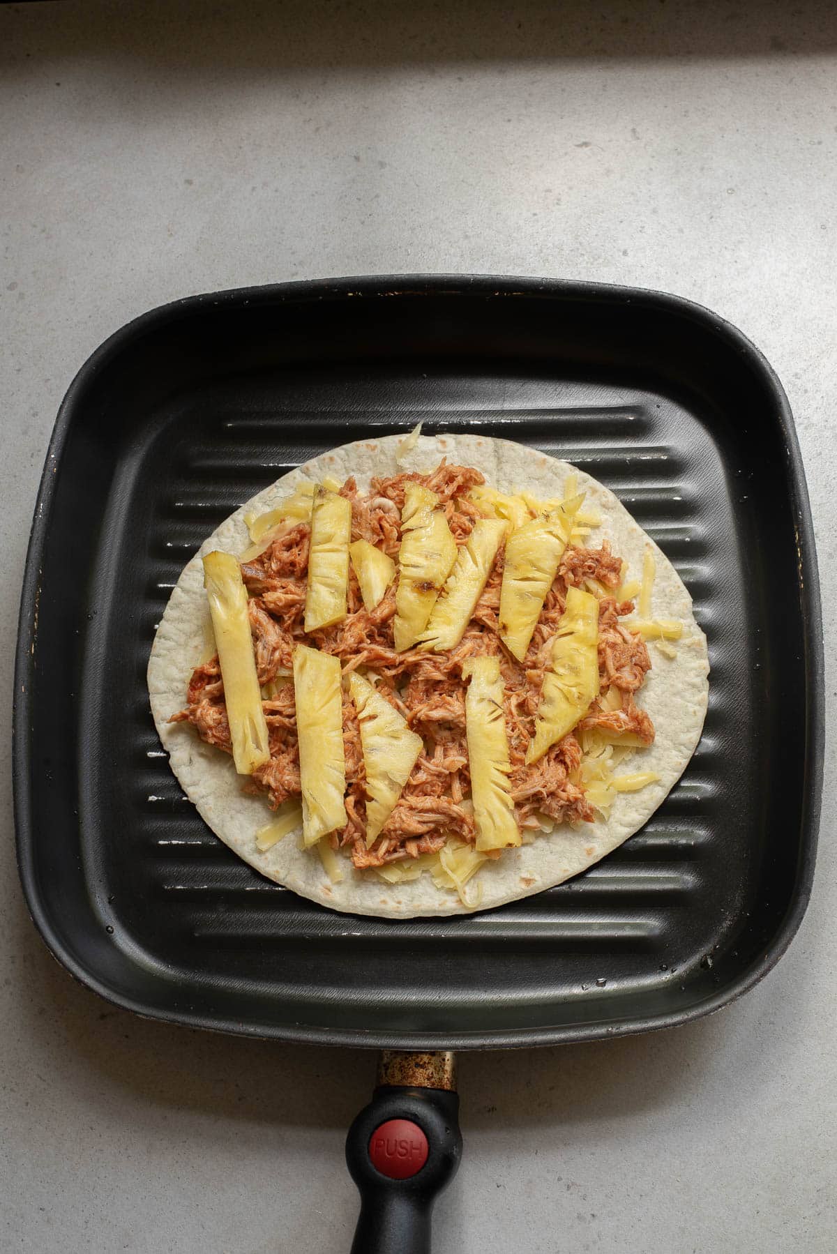 Tortilla with chicken and cheese with pineapple strips on a griddle.