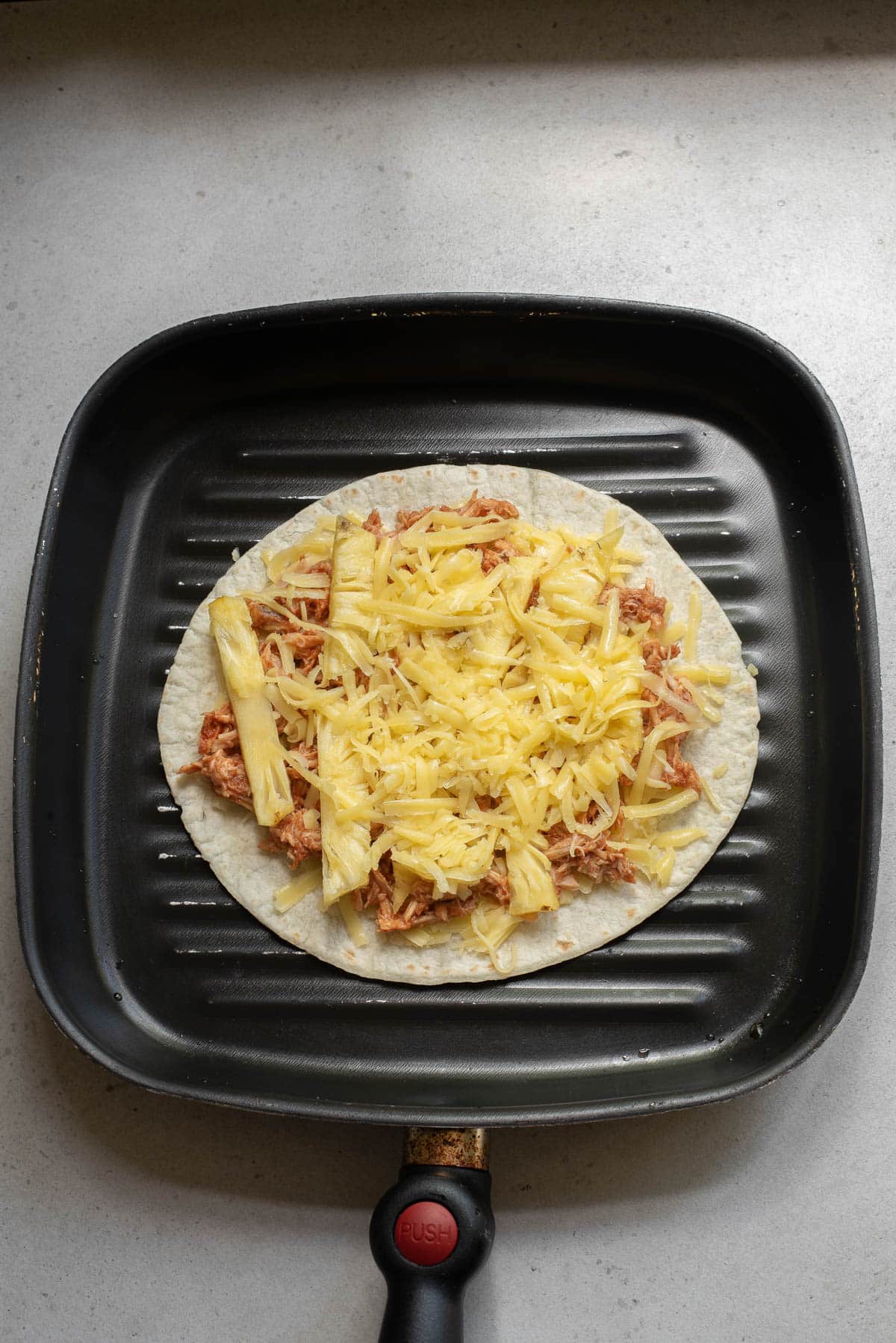 Tortilla with chicken, pineapple, and cheese on a griddle.