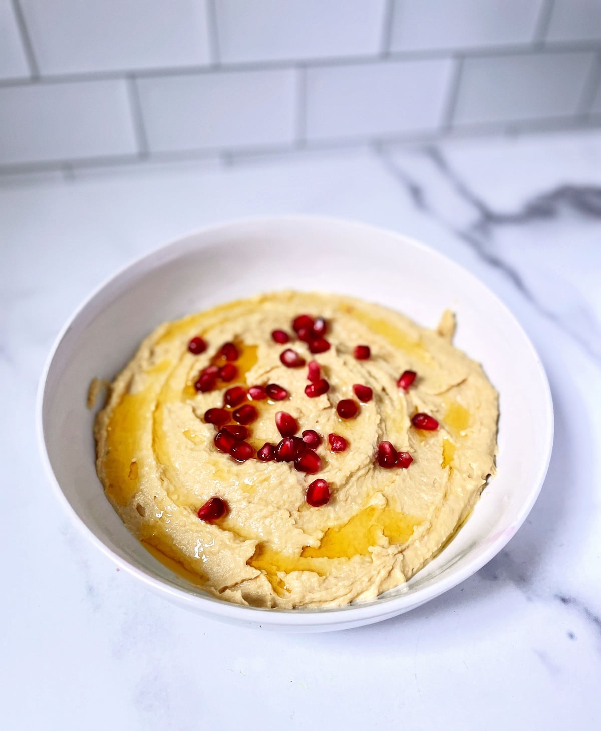 Hummus with olive oil and pomegranate seeds in white bowl.