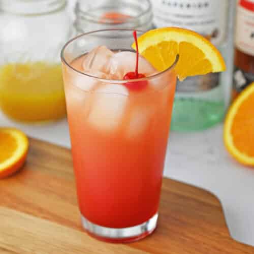 Tropical drink in a tall glass with a cherry and orange slice.