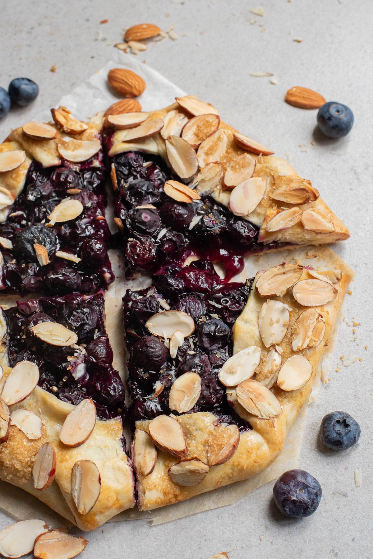 Baked blueberry galette cut in four pieces on parchment paper.