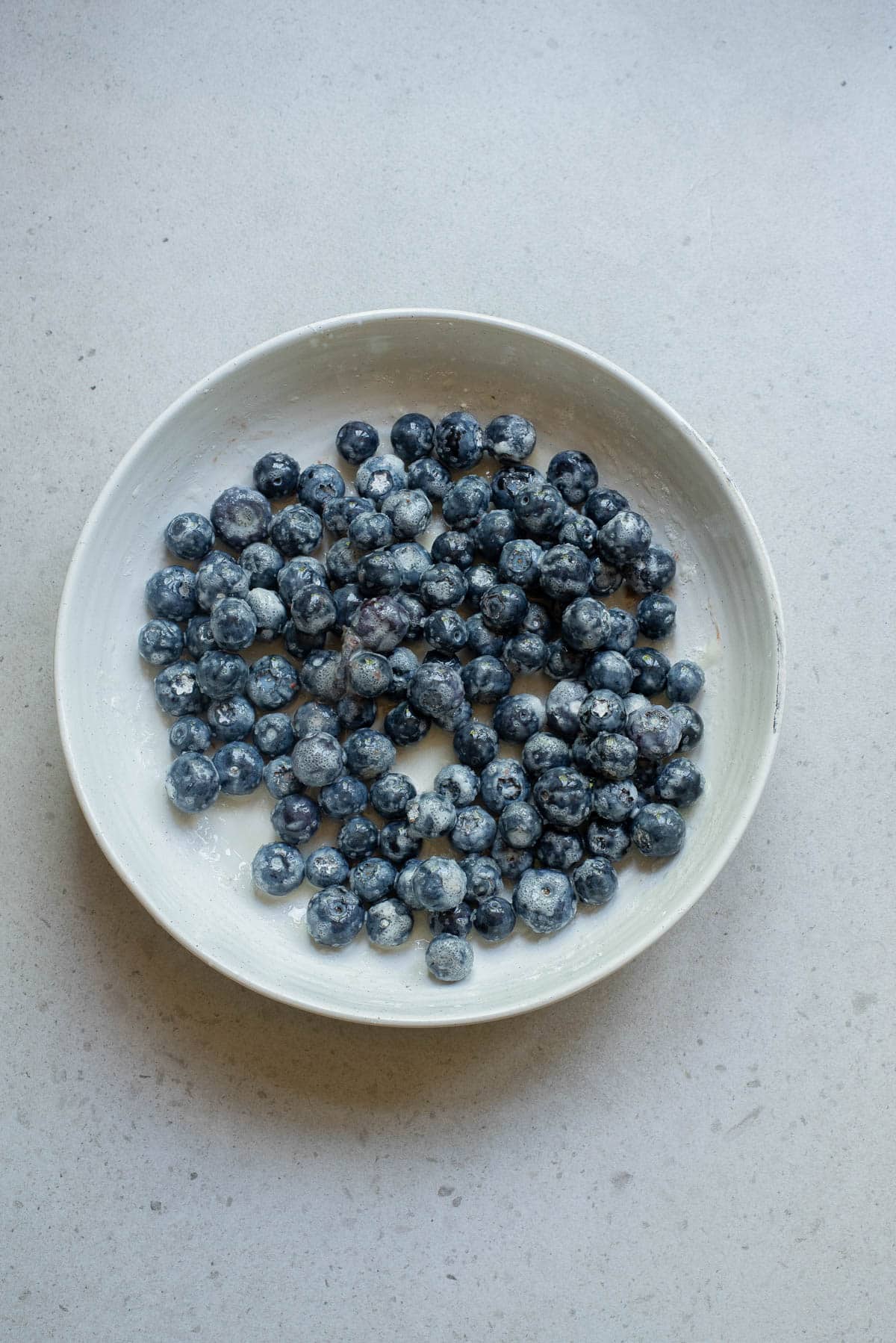 Blueberries with cornstarch, sugar, and lemon juice in a white bowl.