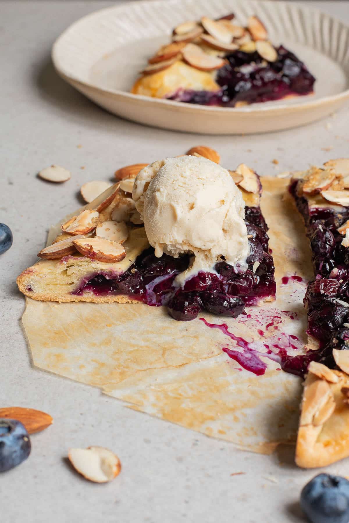 Baked blueberries in a pie crust on parchment paper sprinkled with almonds and topped with ice cream.