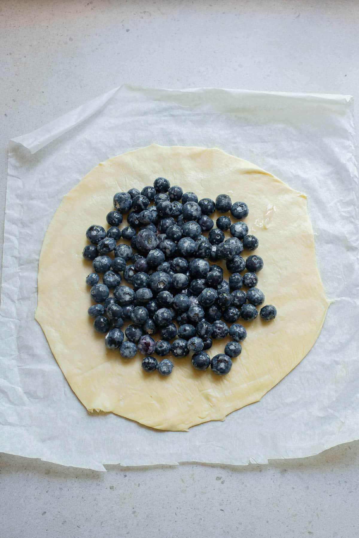 Blueberries on a pie crust on parchment paper.