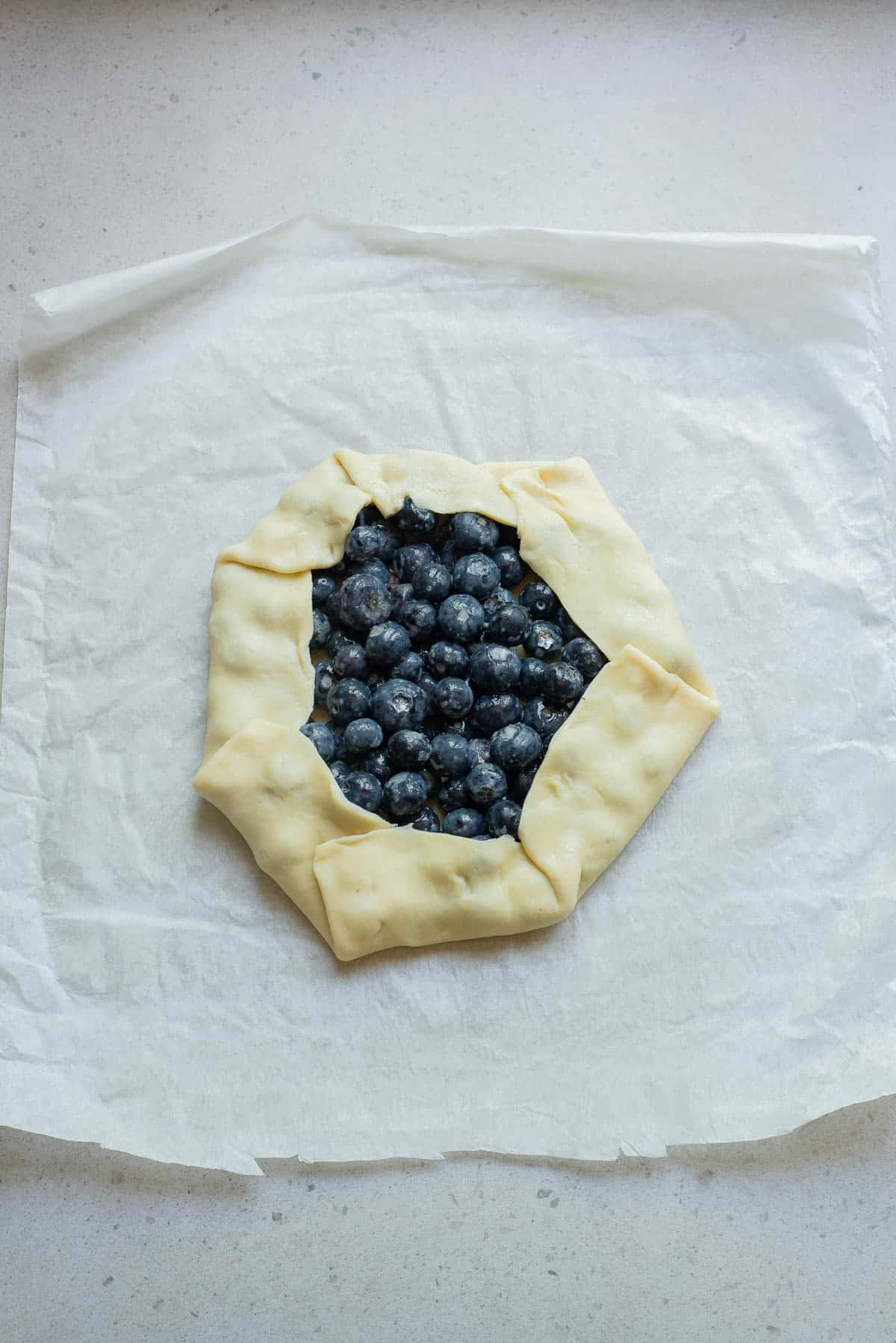 Blueberries on a pie crust  with edge folded up on parchment paper.