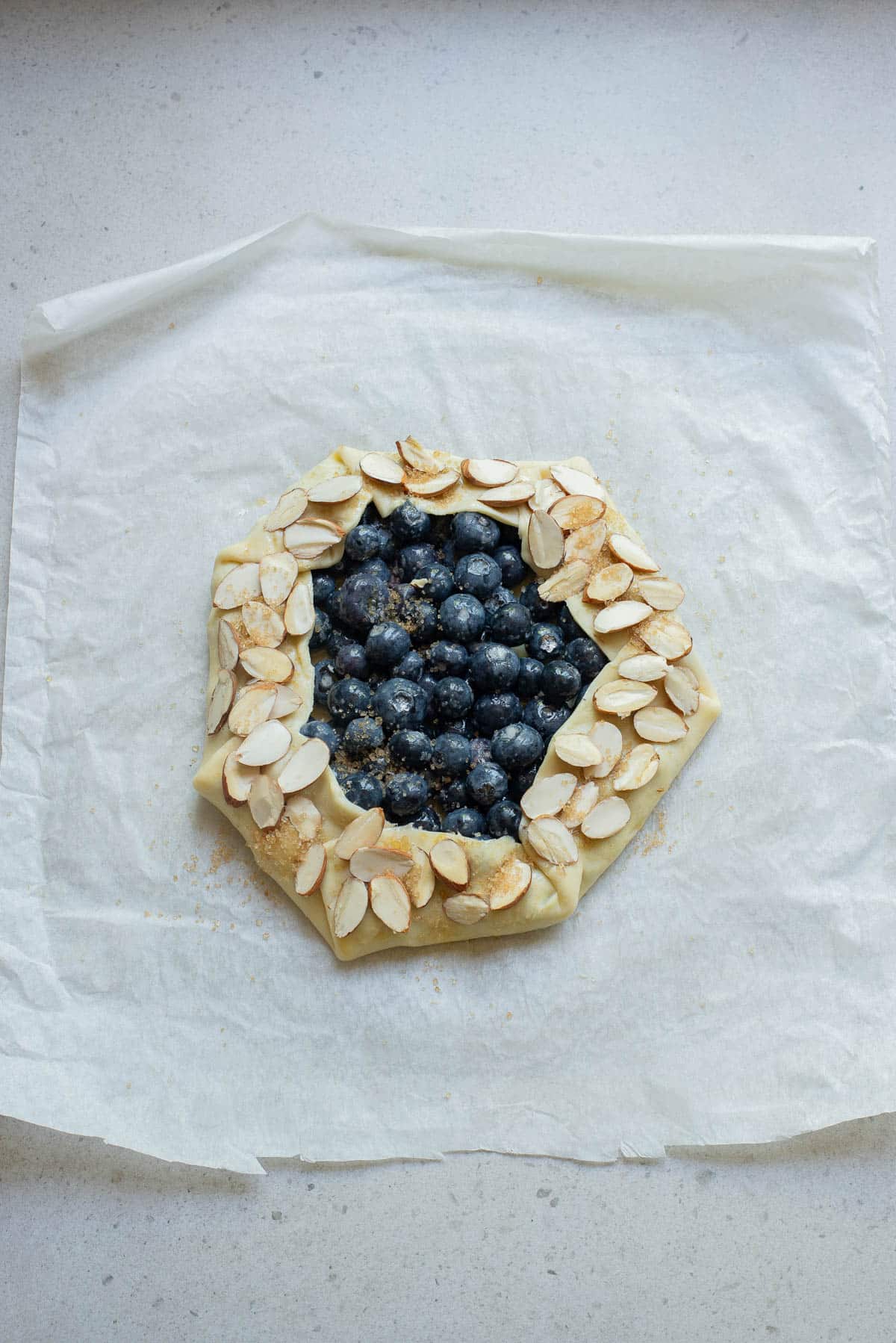Blueberries in a pie crust on parchment paper sprinkled with almonds.