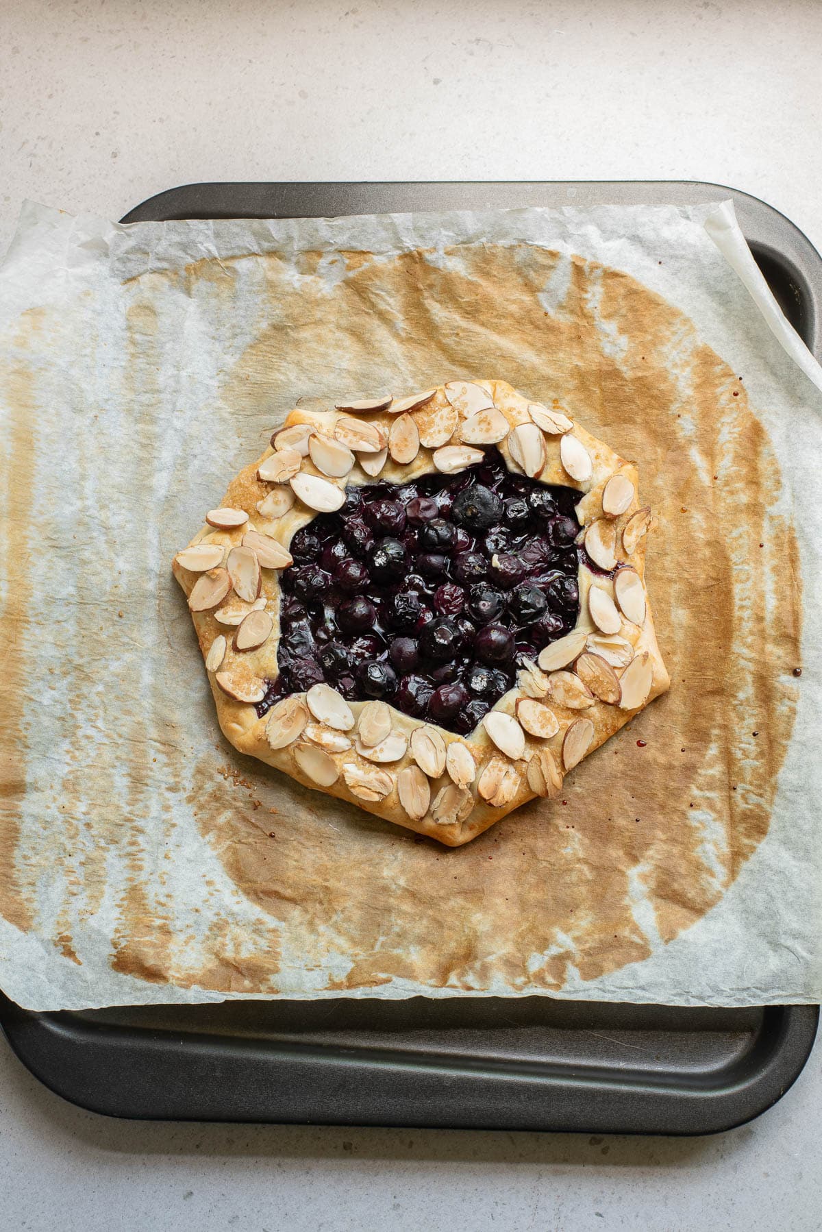 Baked blueberries in a pie crust on parchment paper sprinkled with almonds.