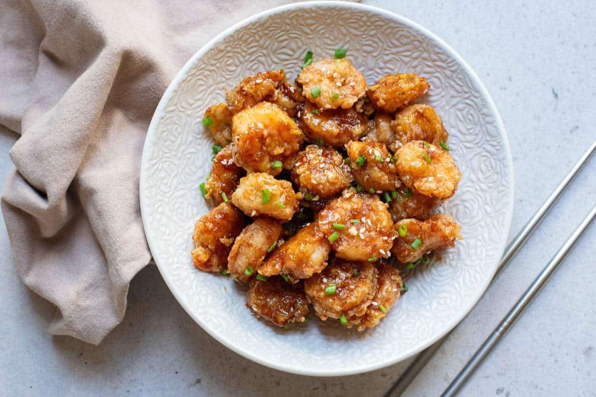 Fried shrimp with sauce and sesame seeds and chives in white bowl.