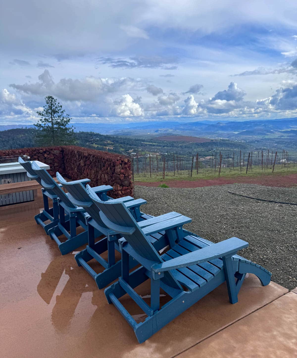 Blue Adirondack chairs on patio with view of vineyard and mountains.