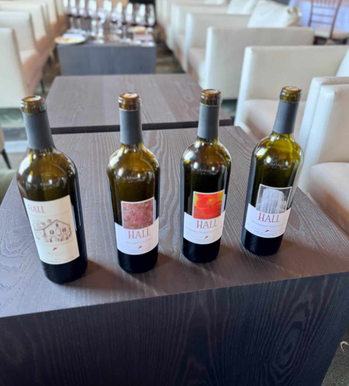 Four bottles of red wine on table between chairs.