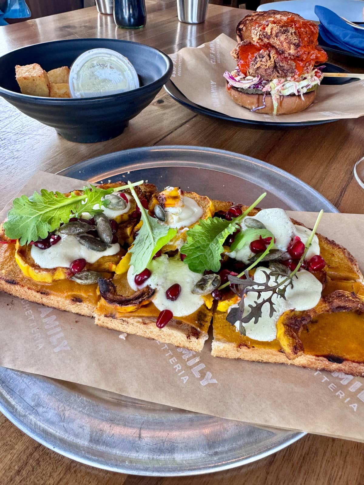 Squash flatbread with cheese in front of a fried chicken sandwich and other dish.