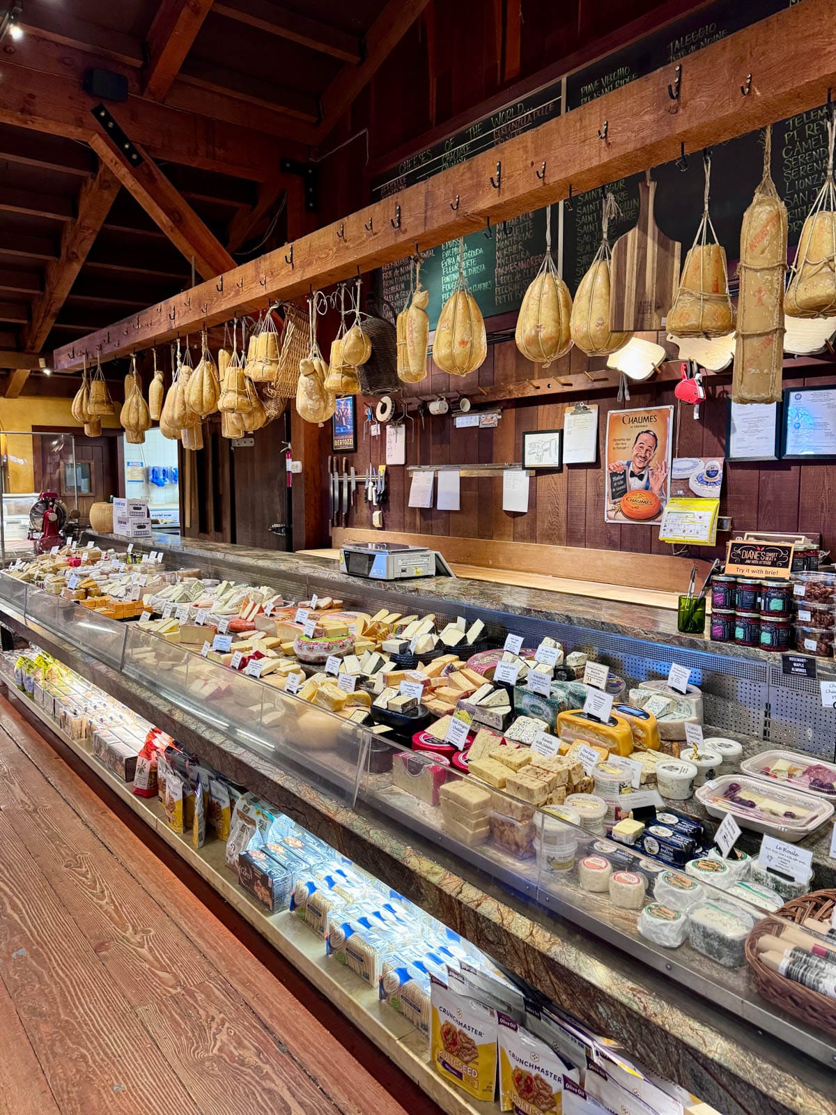 Counter in store with meat hanging above and cheeses in the case.