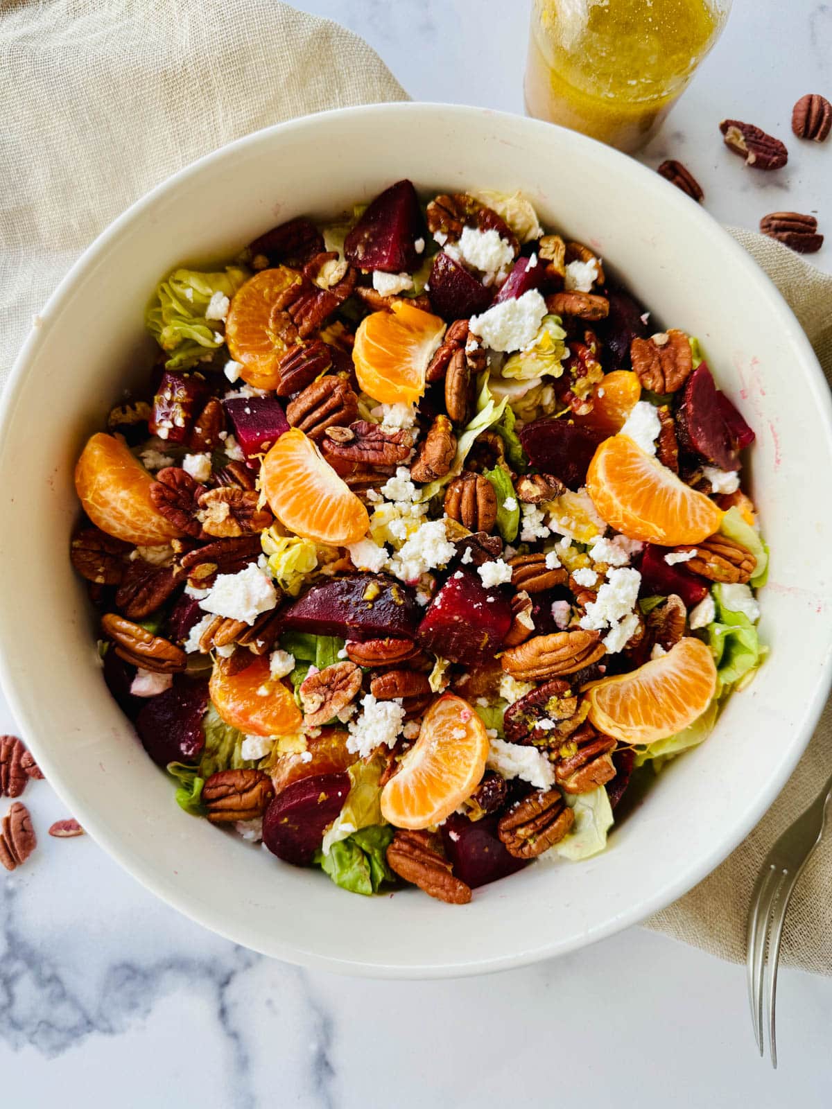 Beets, lettuce, orange slices, feta and pecans in a white bowl on a white marble counter.