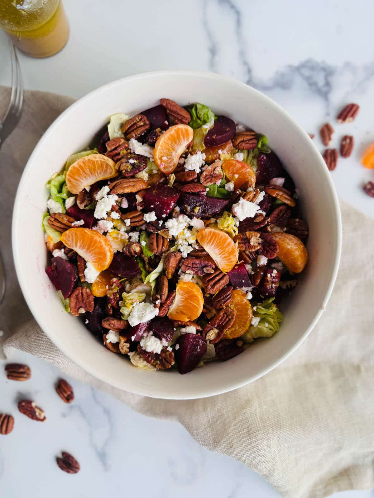 Beet, lettuce, orange sections, feta, and pecans in a white bowl on a white marble counter.