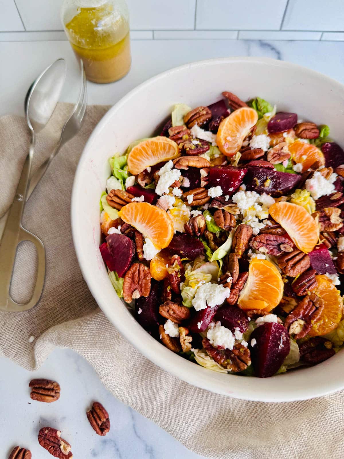 Beet, lettuce, orange sections, feta, and pecans with balsamic dressing in a white bowl.