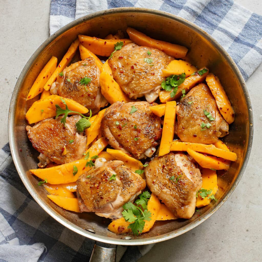 Chicken and mango slices in a pan with cilantro.