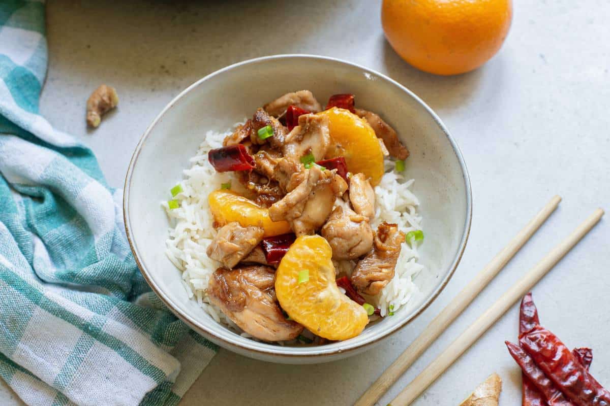 Mandarin chicken over rice in a white bowl with chopsticks.