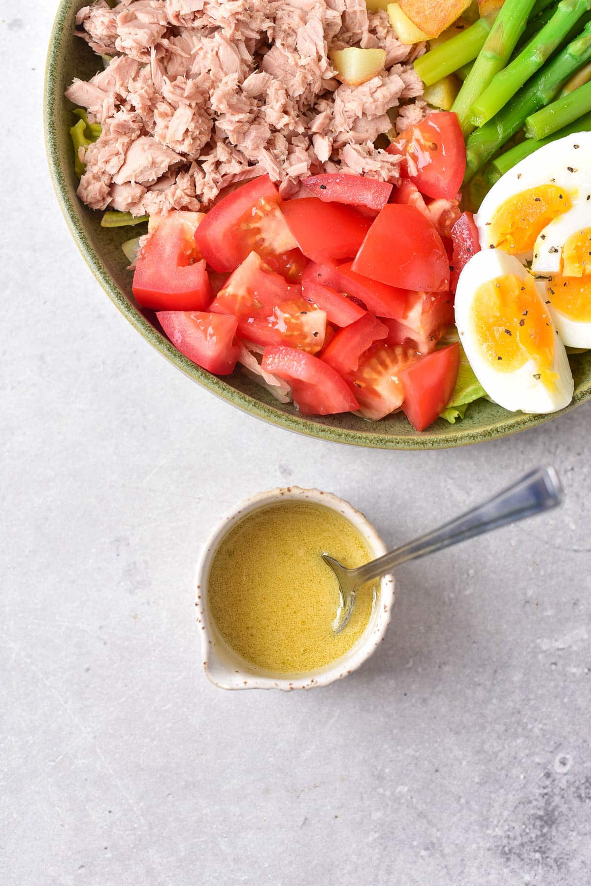 Corner of salad with tomatoes and egg with small cup of salad dressing and small spoon.