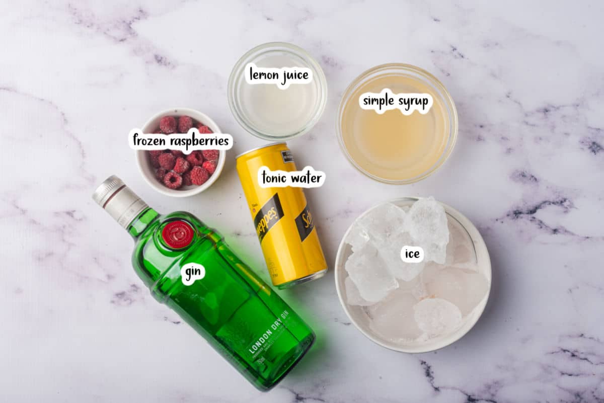 Ingredients to make a frozen raspberry gin and tonic on a white marble counter.