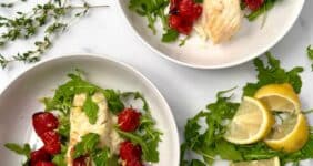 Seared fish served over mashed parsnips with roasted cherry tomatoes and arugula in a white bowl for Pinterest.