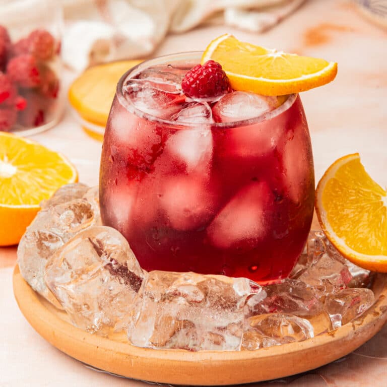 Red wine cocktail over ice in glass with orange slice and raspberry.