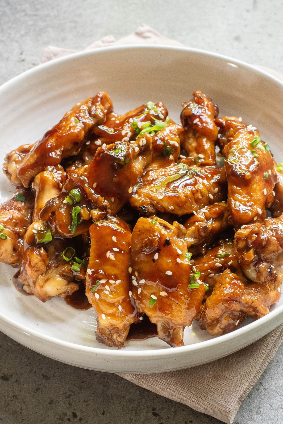 Saucy chicken wings in a white bowl with sesame seeds and green onions.
