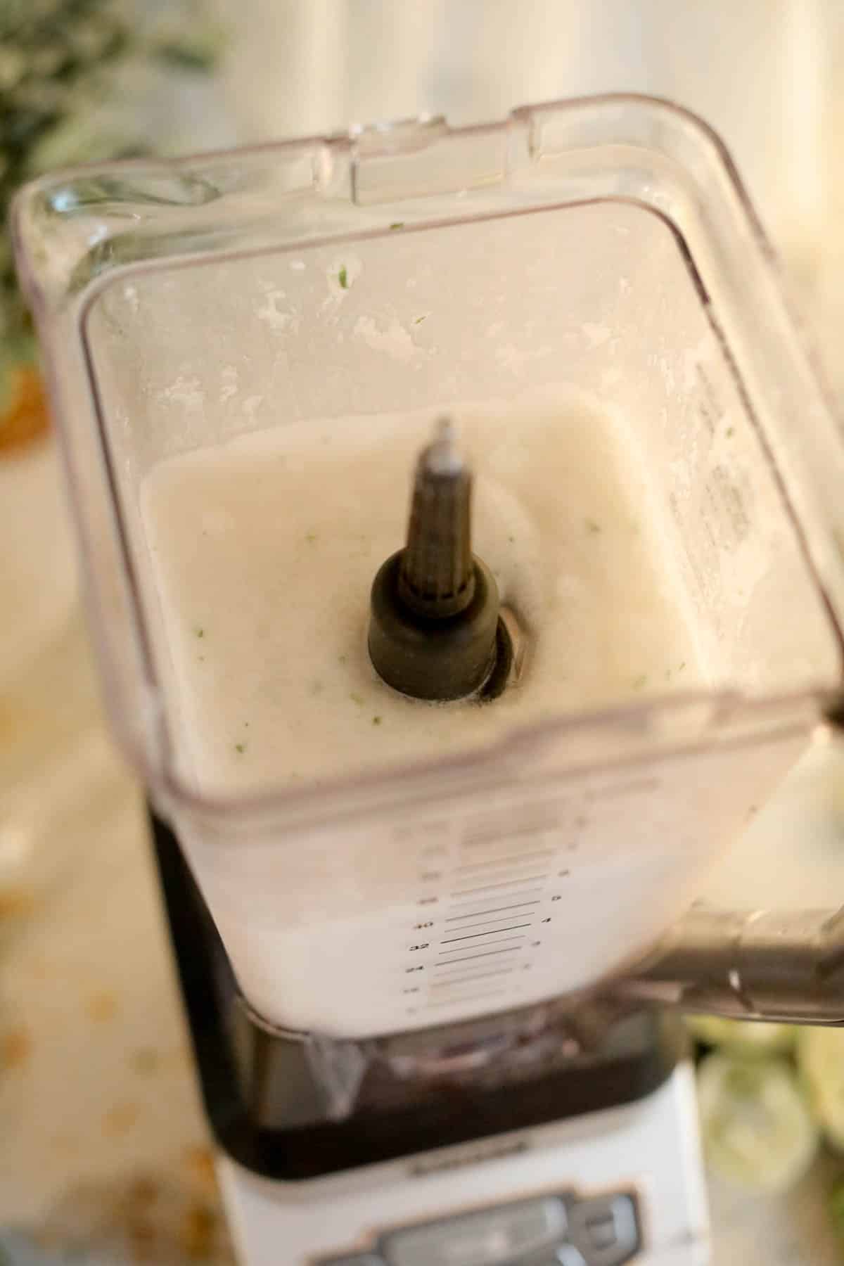 Creamy frozen liquid with lime zest in a blender.