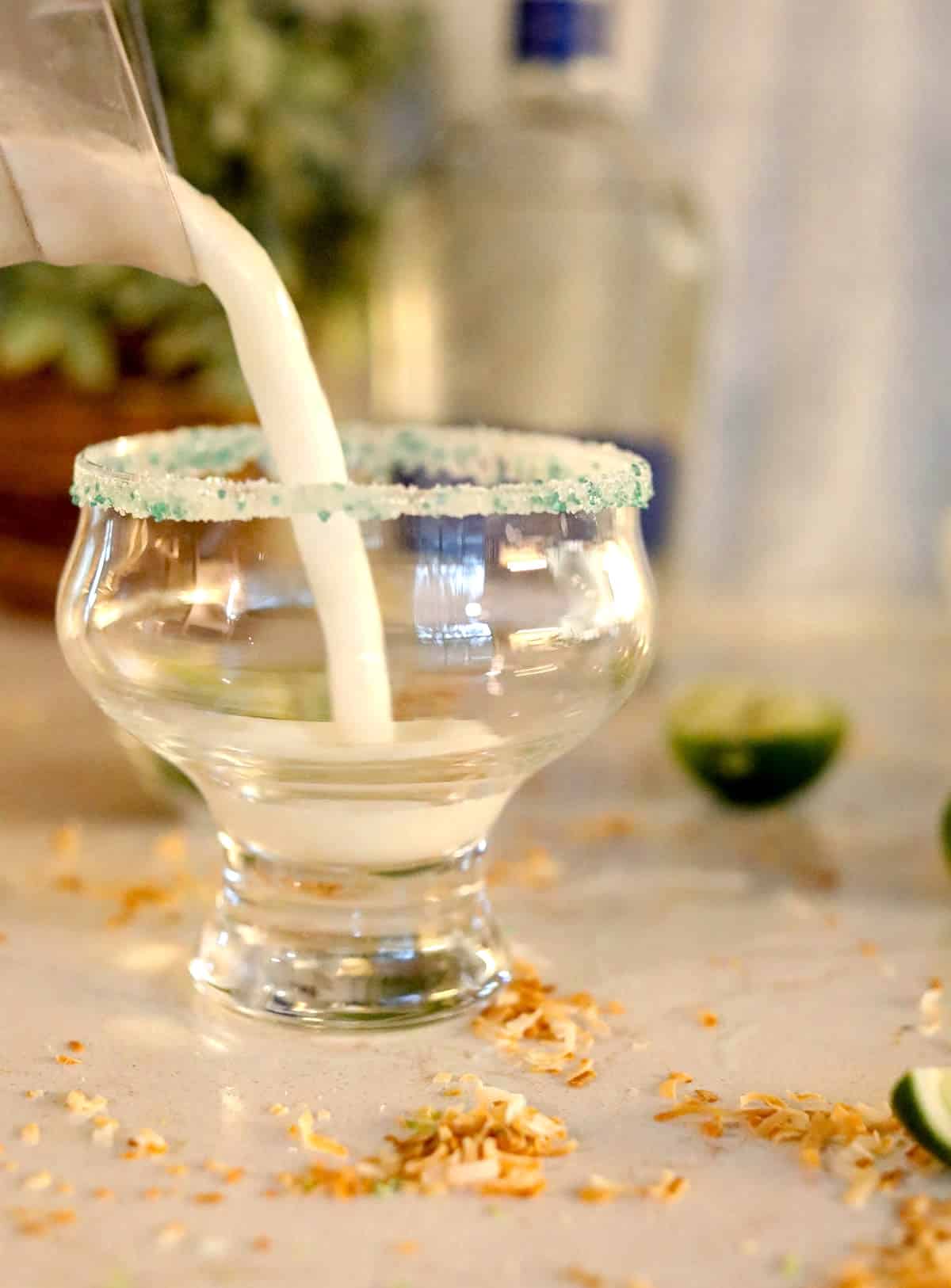 White frozen liquid being poured into a sugar rimmed glass on a beige counter.