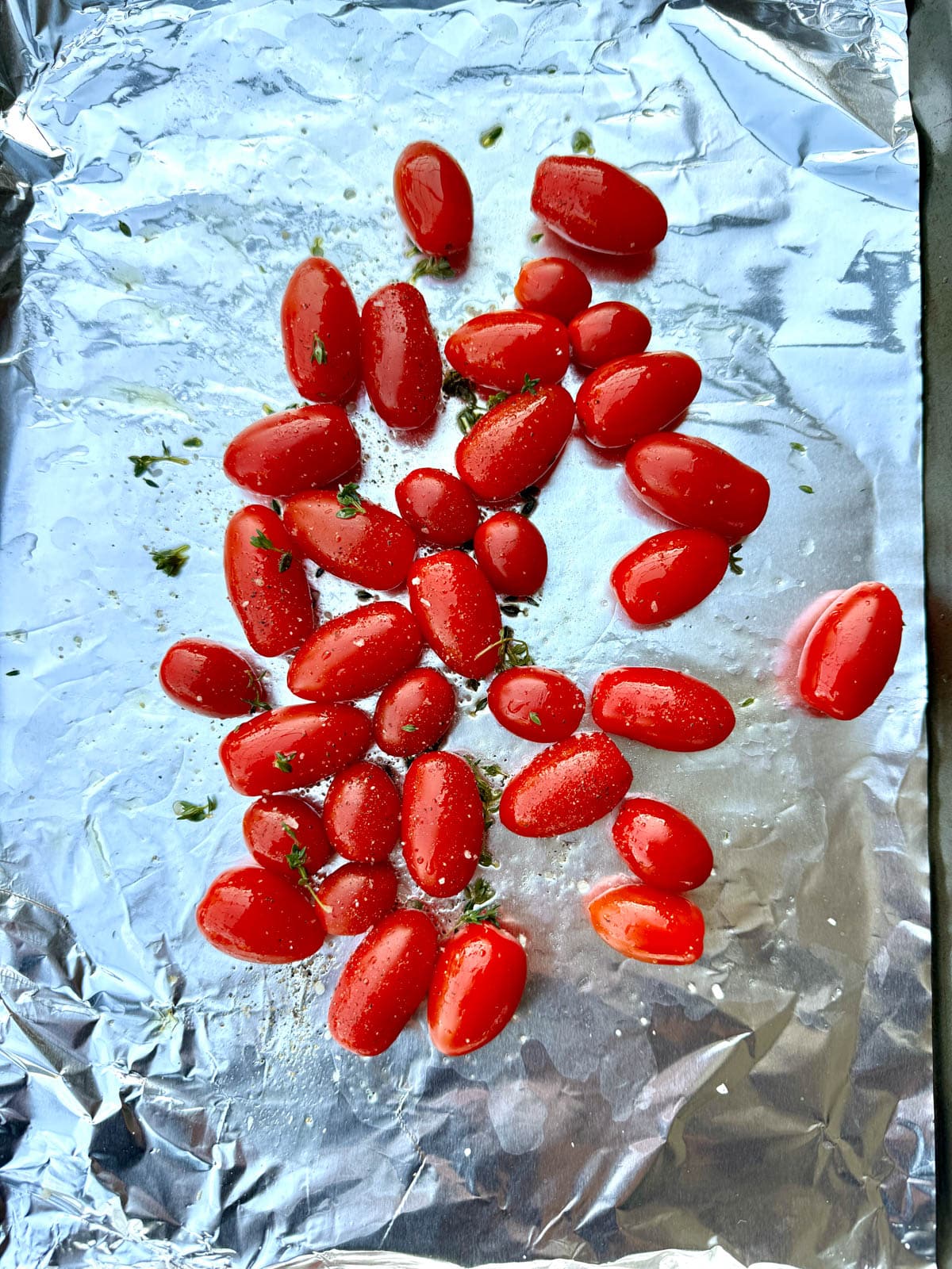 Cherry tomatoes, thyme, and oil on foil on baking sheet.