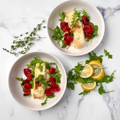 Seared fish served in a white bowl over mashed parsnips with roasted cherry tomatoes and arugula.
