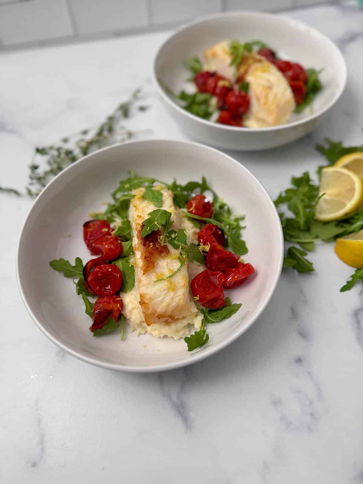 Place the seared fish in a pan in a white bowl over mashed parsnips with roasted cherry tomatoes, arugula and lemon wedges.
