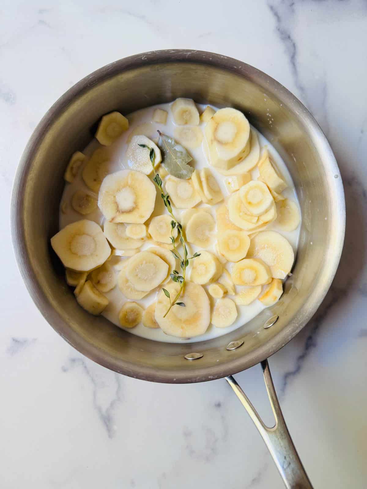 Sliced ​​parsnips and cream placed in a pan on a white marble counter.