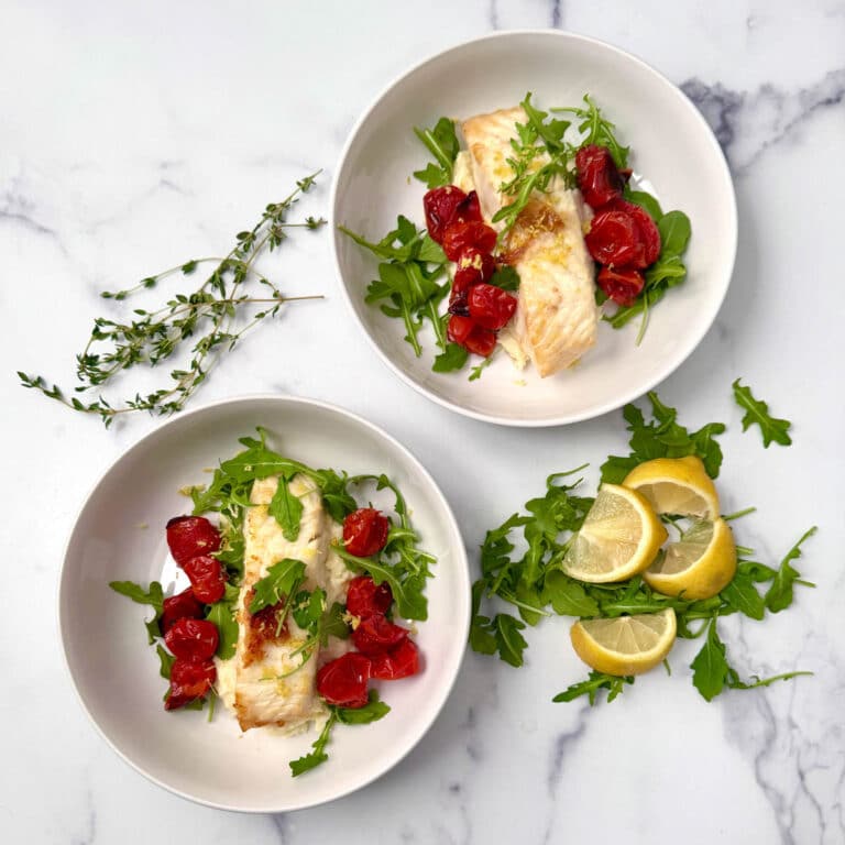 Pan seared fish in white bowls over mashed parsnips with roasted cherry tomatoes and arugula.