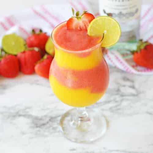 Frozen strawberry and mango daiquiri in a hurricane glass with a bottle of rum in background.